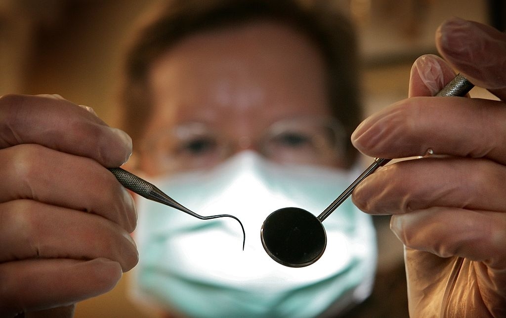 Person in mask holding dental tools, magnifying glass in front of one eye