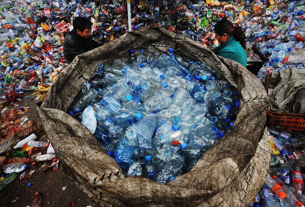 Two individuals sorting through a large collection of plastic bottles for recycling