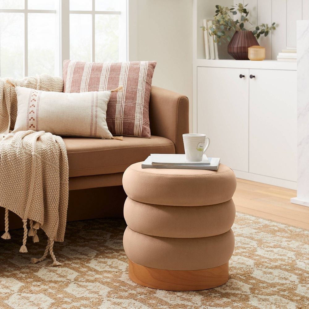 A modern living room with a couch, a layered round ottoman, a throw blanket, a cushion, and a side cabinet