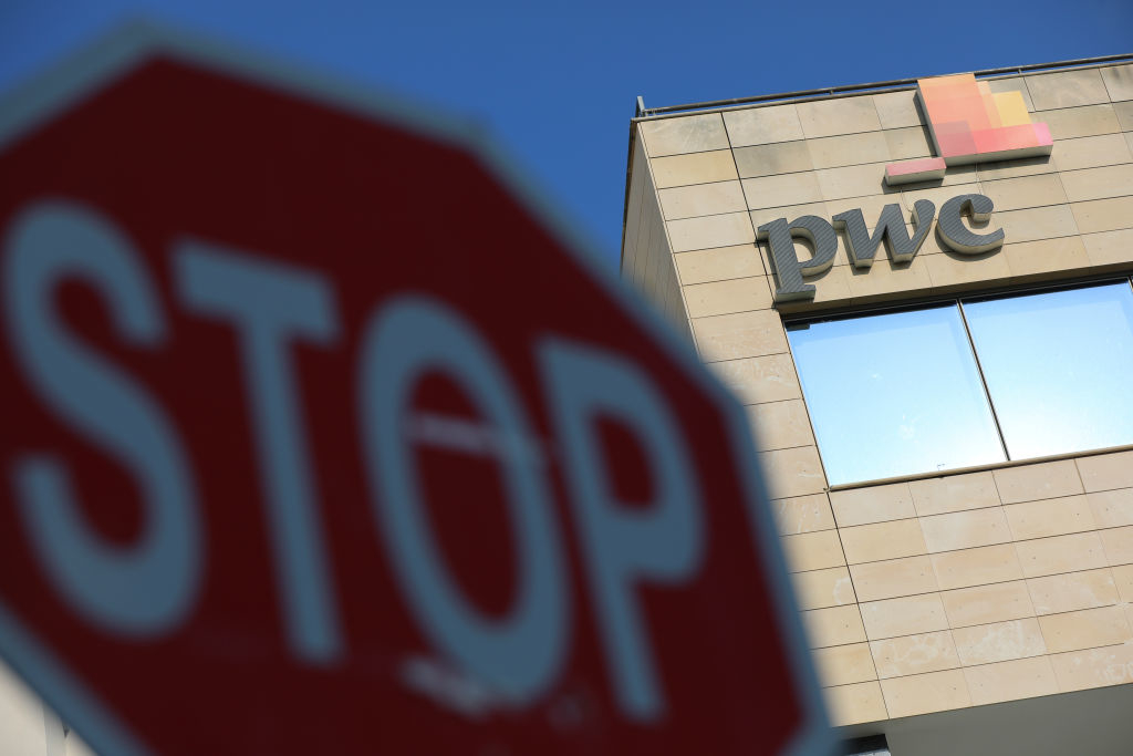 A stop sign in the foreground with the PwC company logo on a building in the background