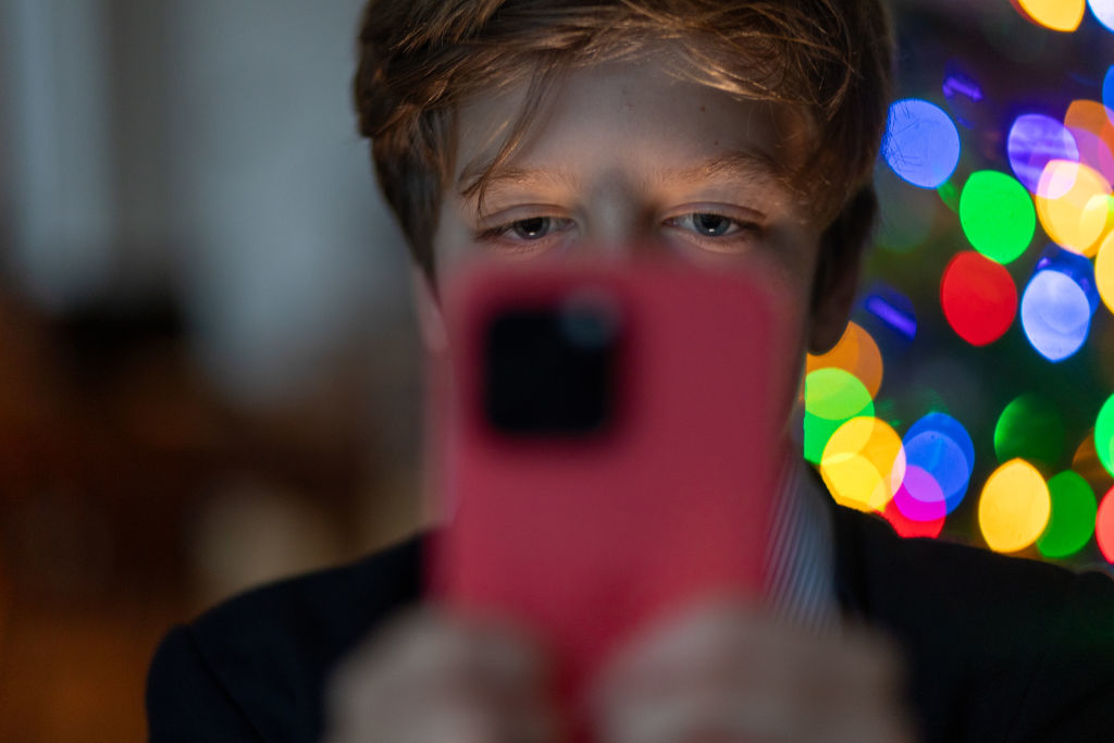 Person taking a selfie with a phone, blurred colorful lights in the background. Name not provided
