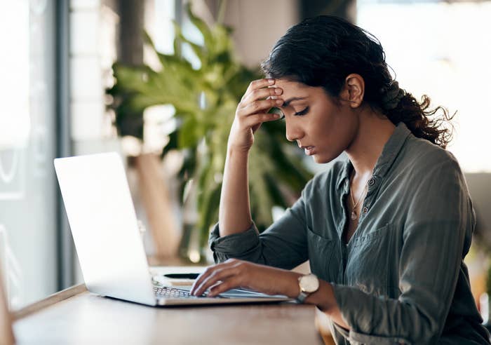 Woman looking stressed at a laptop, holding her forehead, possibly dealing with work issues