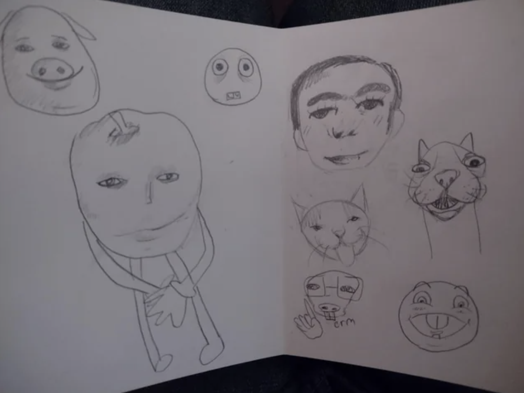 A sketchbook open to a page with hand-drawn doodles of various cartoonish faces and animals