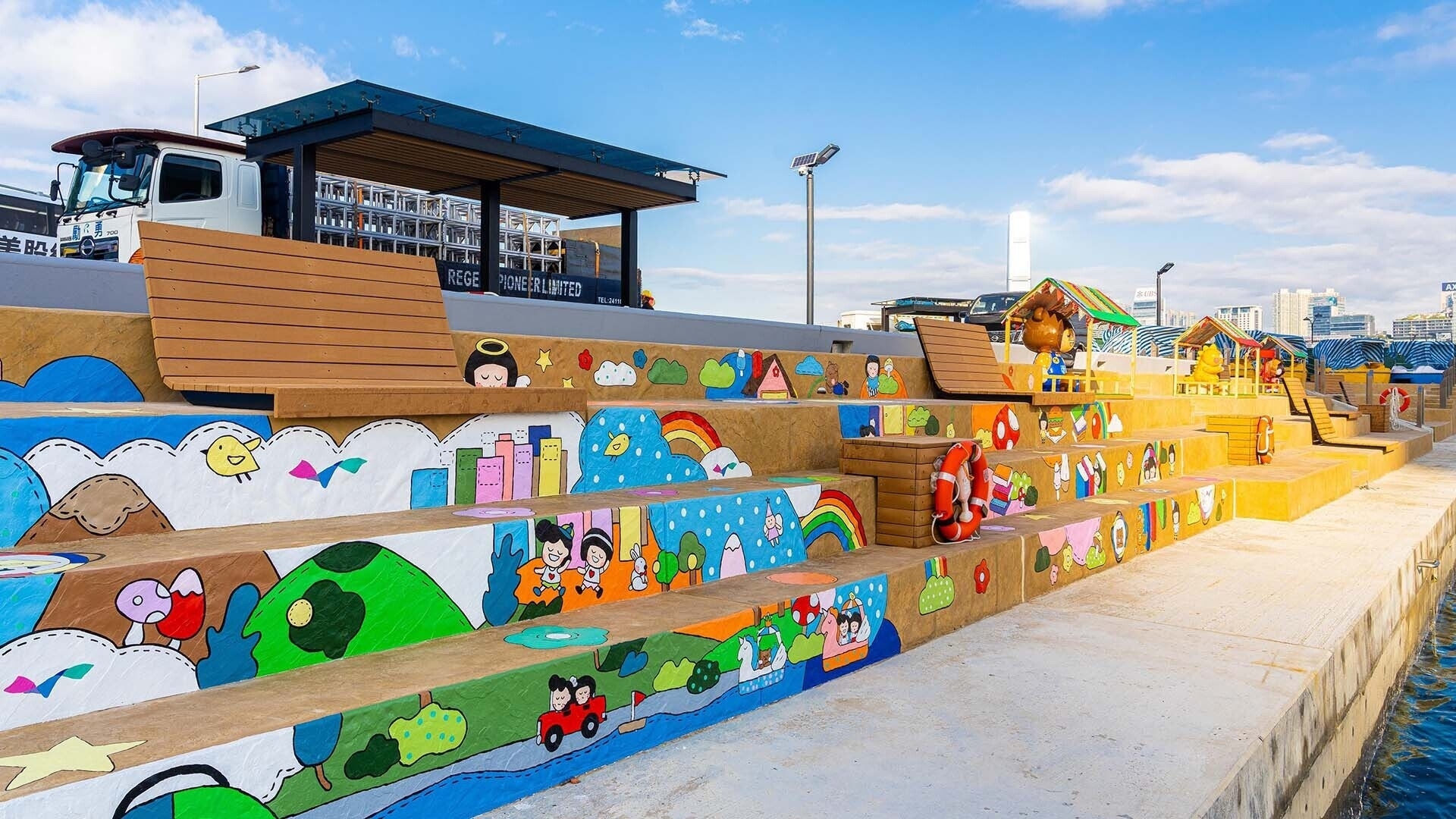 A seaside boardwalk featuring steps painted with colorful, child-friendly illustrations and a small, roofed boat in the background