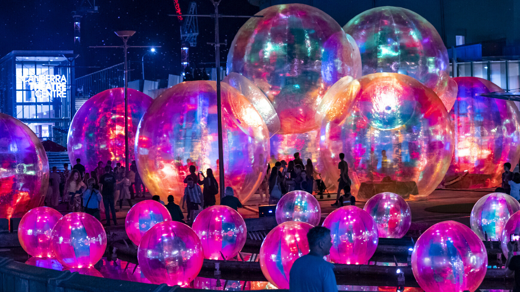 People walking among large illuminated translucent spheres at night