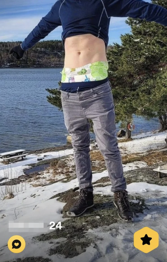 Person wearing a shirt that&#x27;s raised, showing their bare chest, with their pants down around their hips, showing their underwear, jumping mid-air, with their face obscured and snowy lakeside view in the background