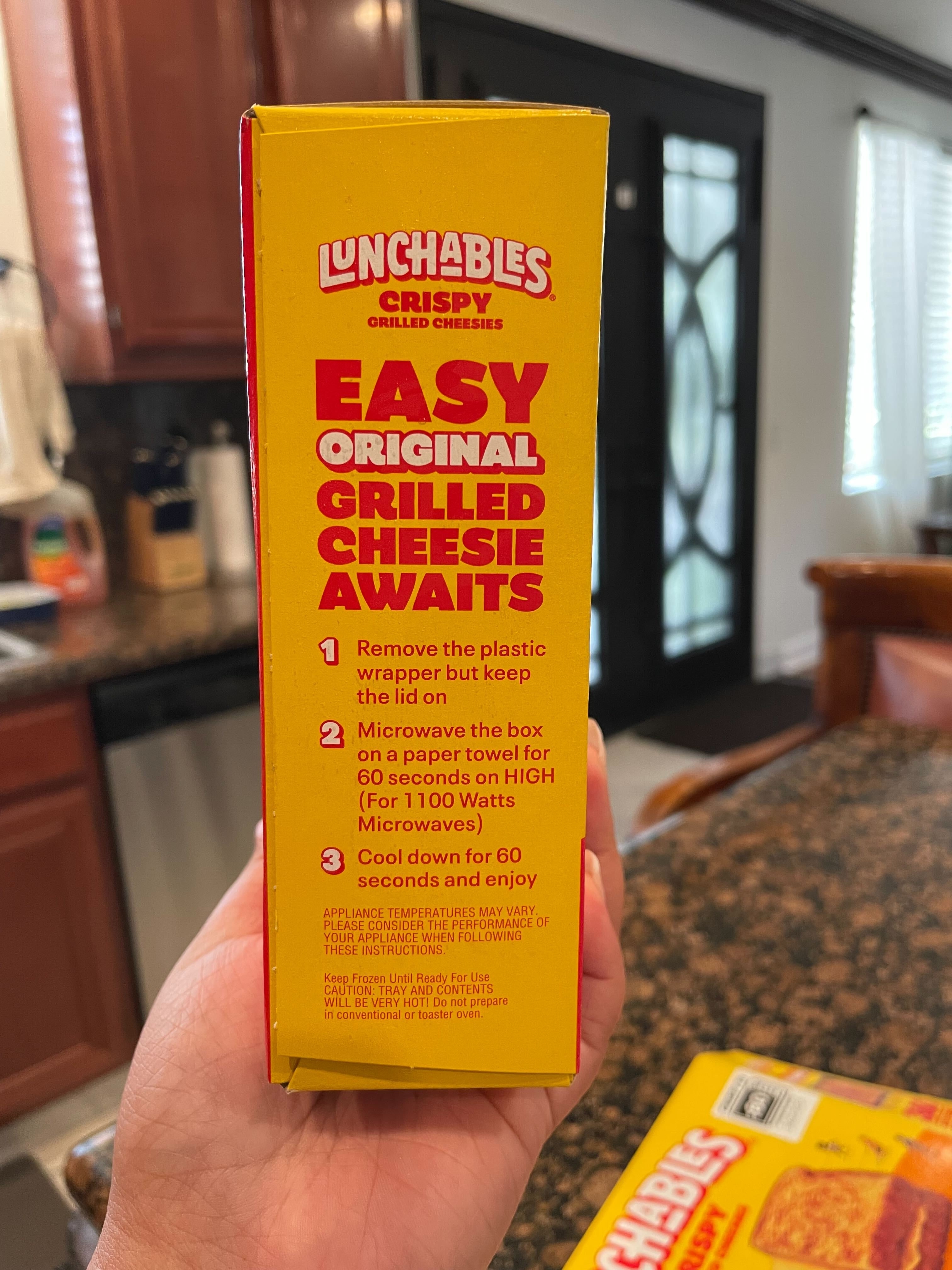 A hand holding a Lunchables Grilled Cheesies box with instructions on how to prepare the meal