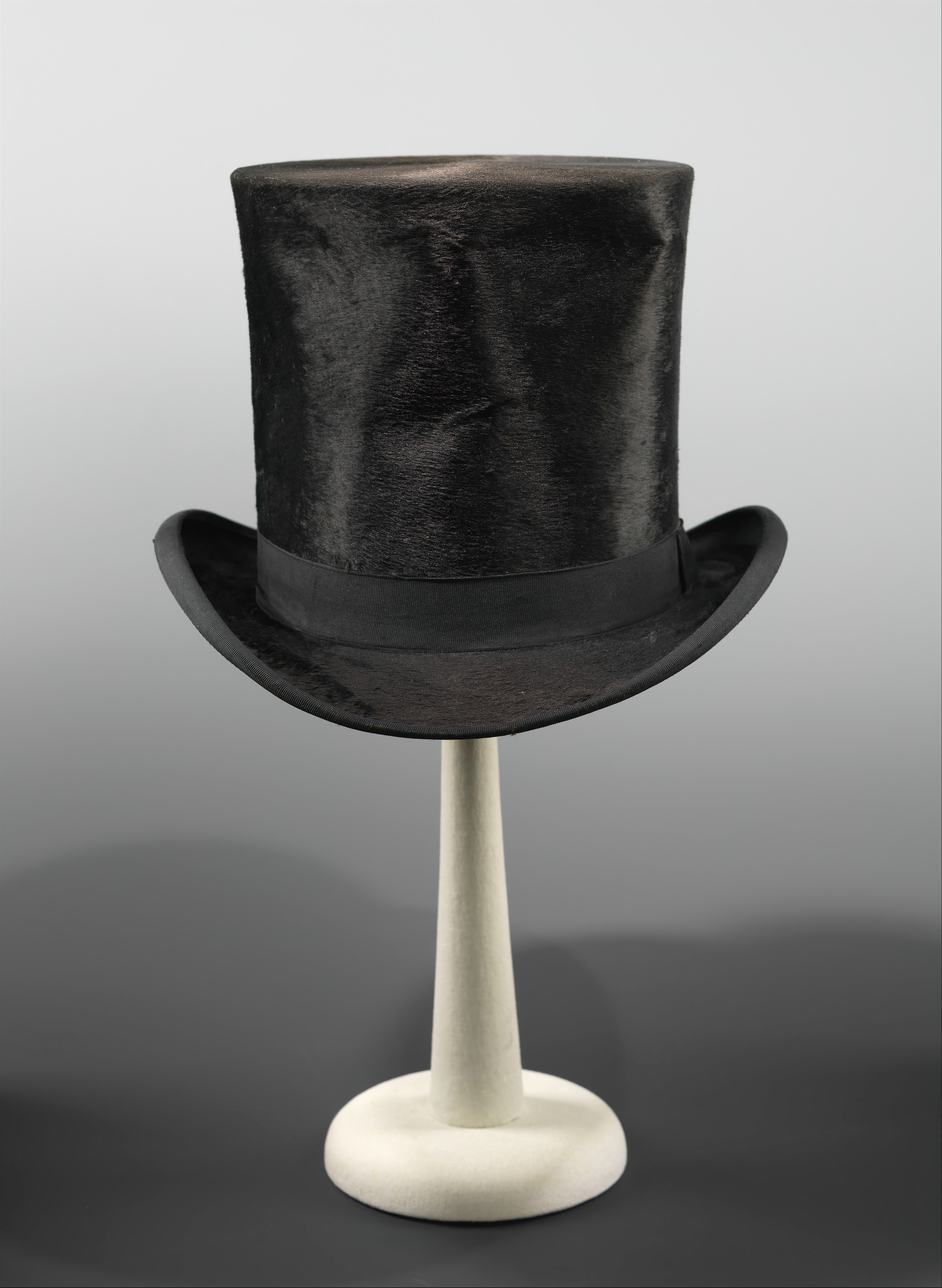 A vintage top hat displayed on a stand with a neutral background