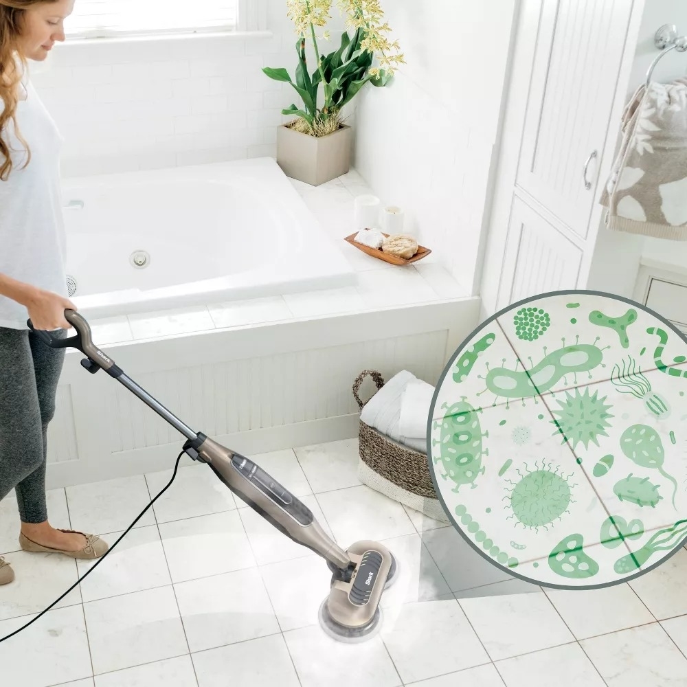 Person using a steam mop to clean a bathroom floor; the device&#x27;s efficacy is highlighted with a germ visualization circle