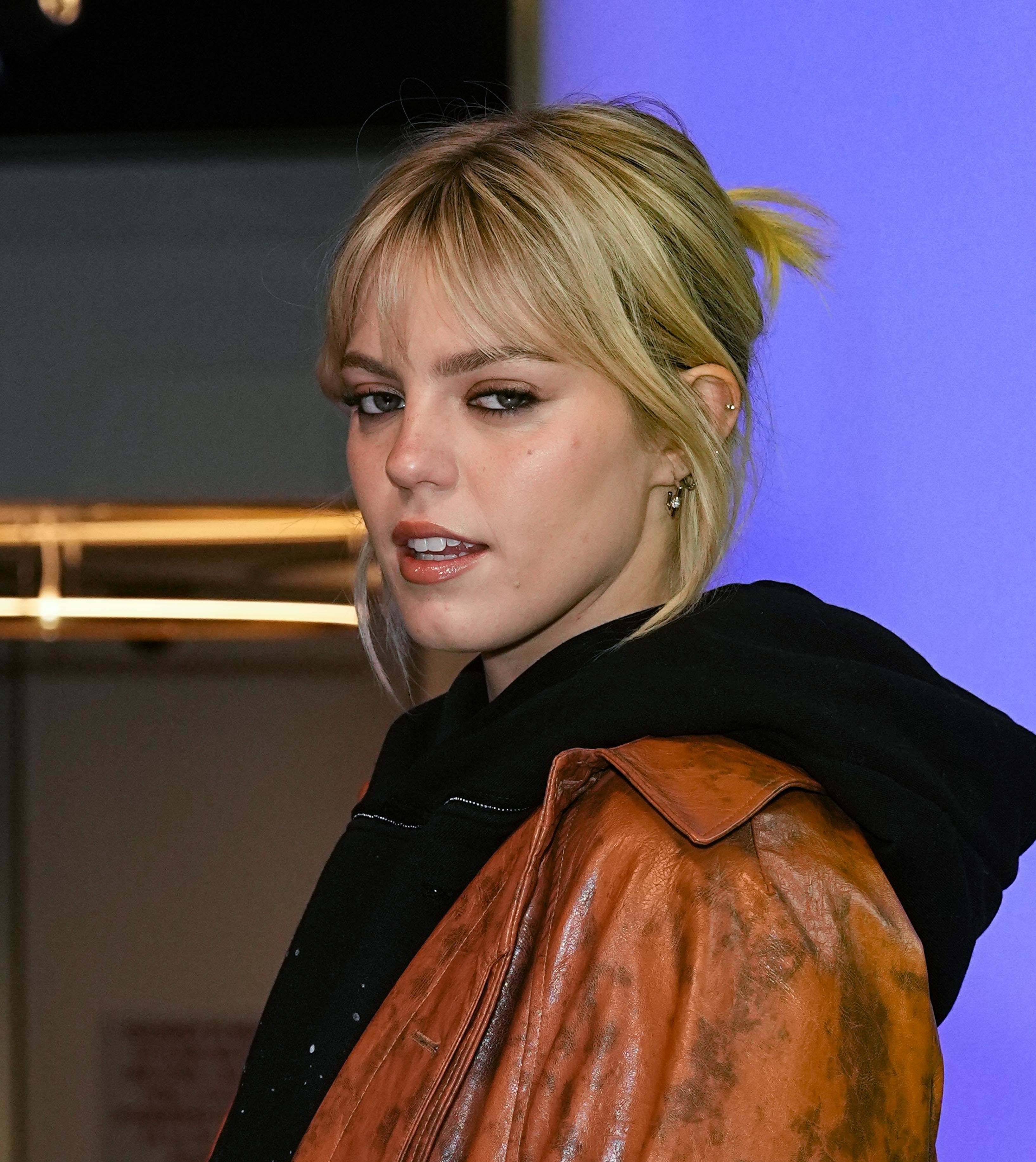 Reneé Rapp wearing a leather jacket with a messy bun hairstyle, facing sideways