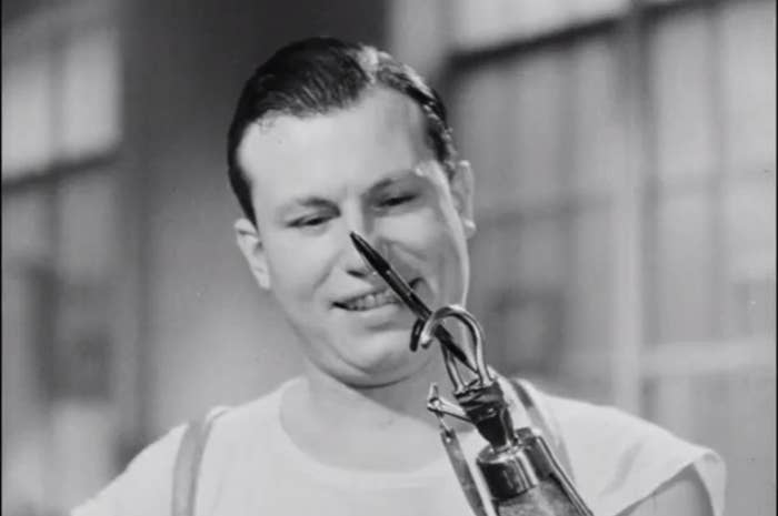 Man in a white tank top operating a robotic hand to hold a cigarette