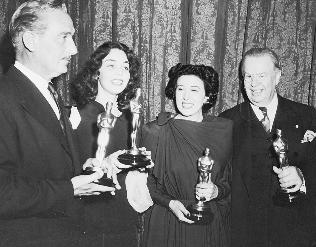 Four people in formal attire holding Oscar statuettes