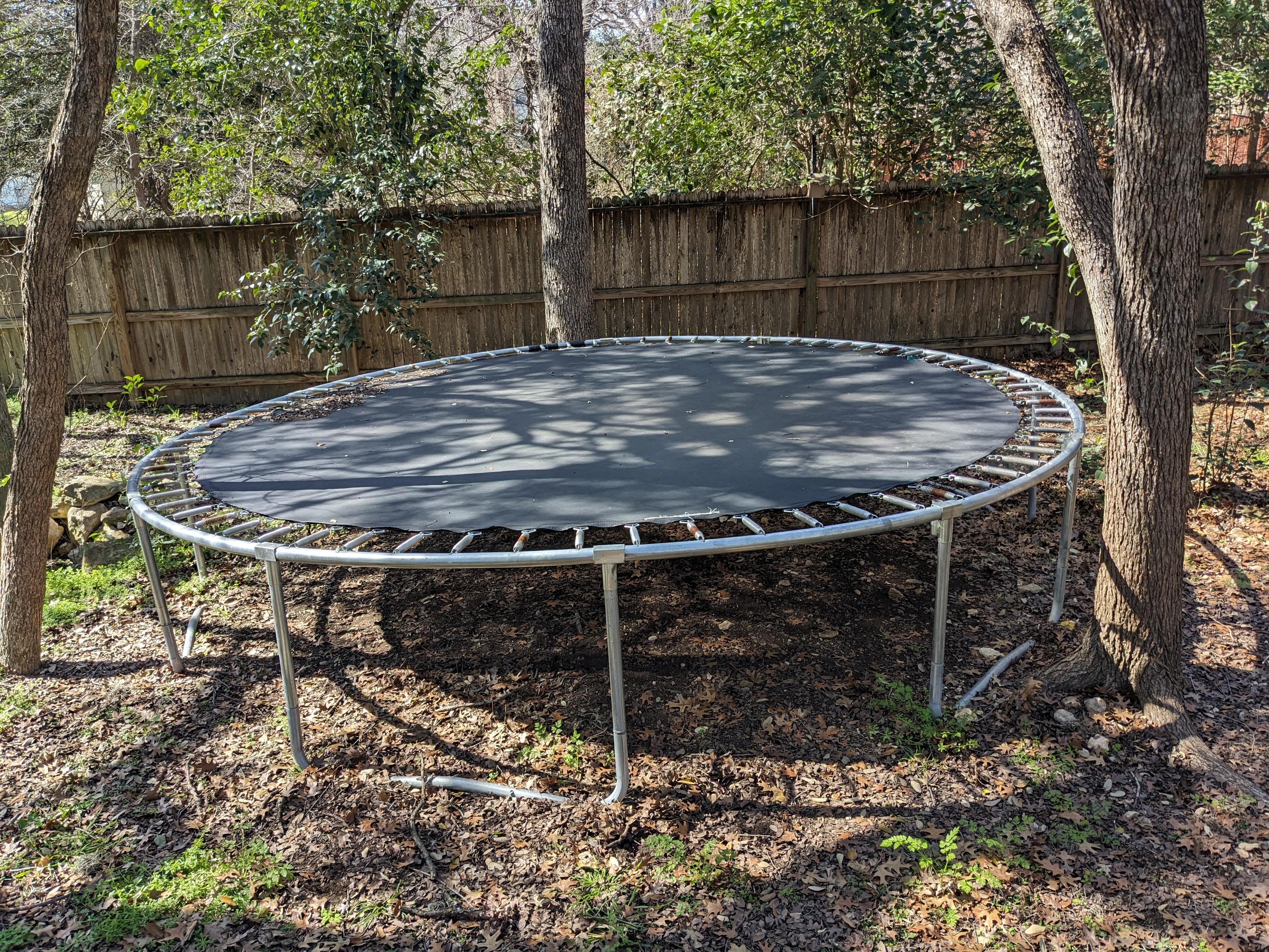 Round trampoline with safety net, set on grass between trees, no people visible