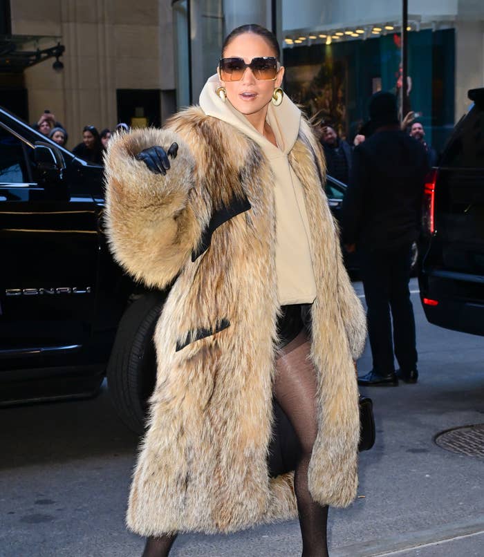Jennifer Lopez in a fur coat, large sunglasses, and black tights exiting a vehicle