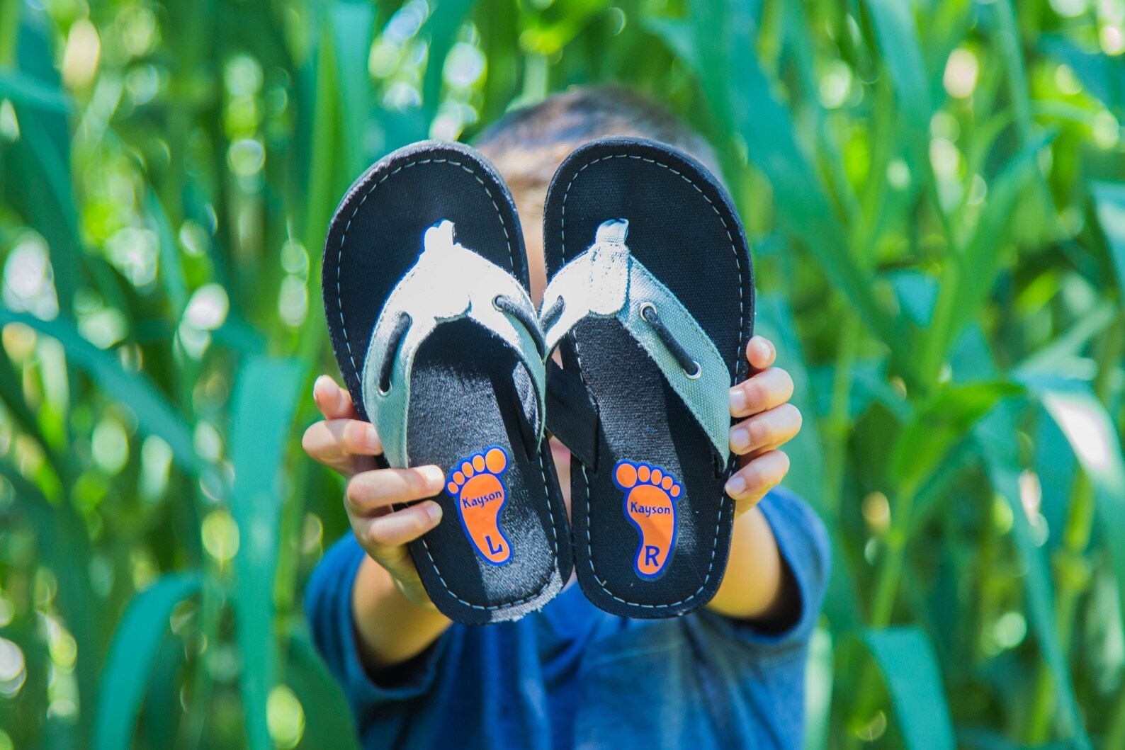 Child holding up a pair of flip-flops with marked foot shapes and &#x27;L&#x27; and &#x27;R&#x27; for left and right feet