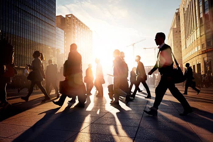 Pedestrians crossing the street in a busy city against a backdrop of buildings and sunlight