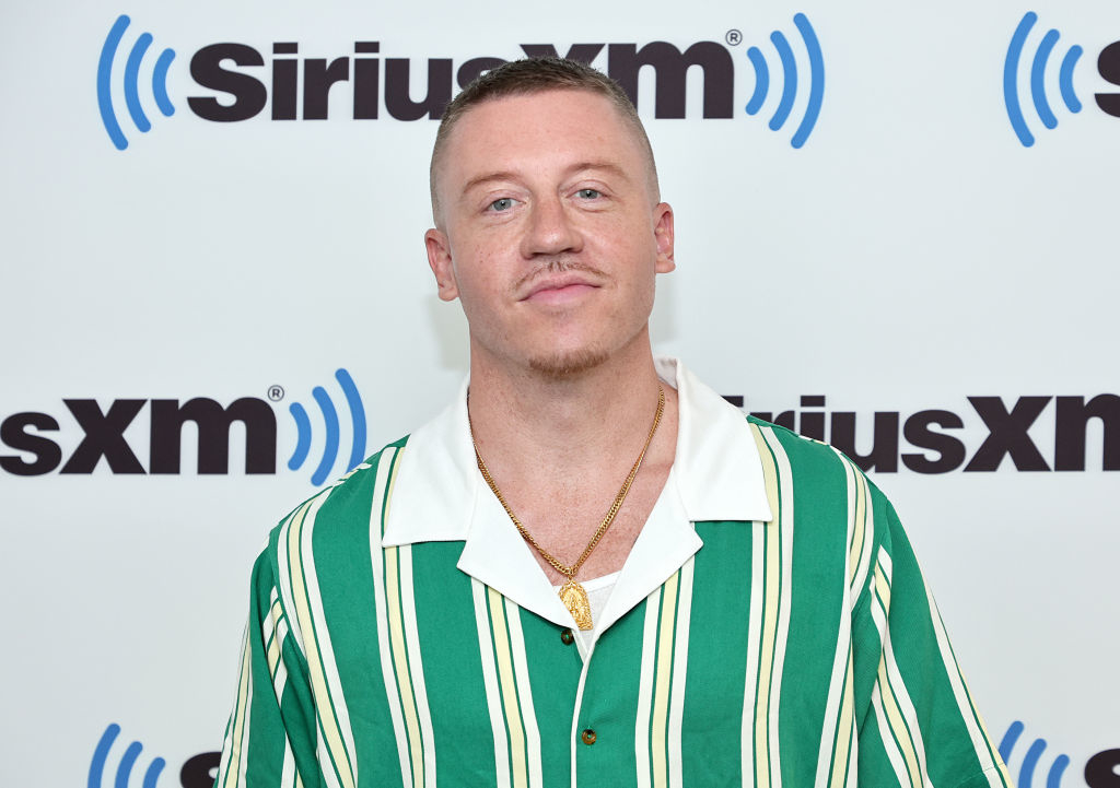 Macklemore in striped shirt and chain necklace standing against a SiriusXM backdrop on the red carpet