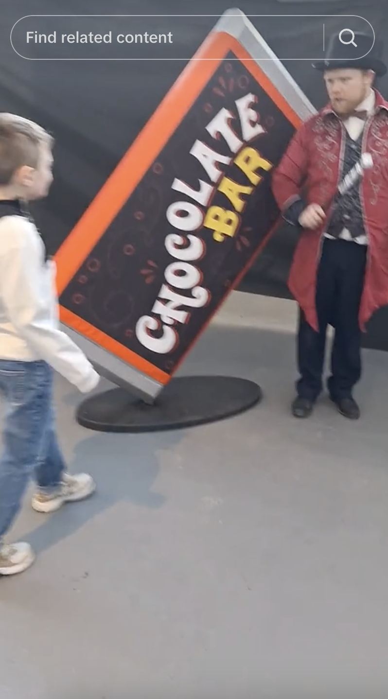 A child interacts with a person dressed as Willy Wonka standing next to an oversized chocolate bar