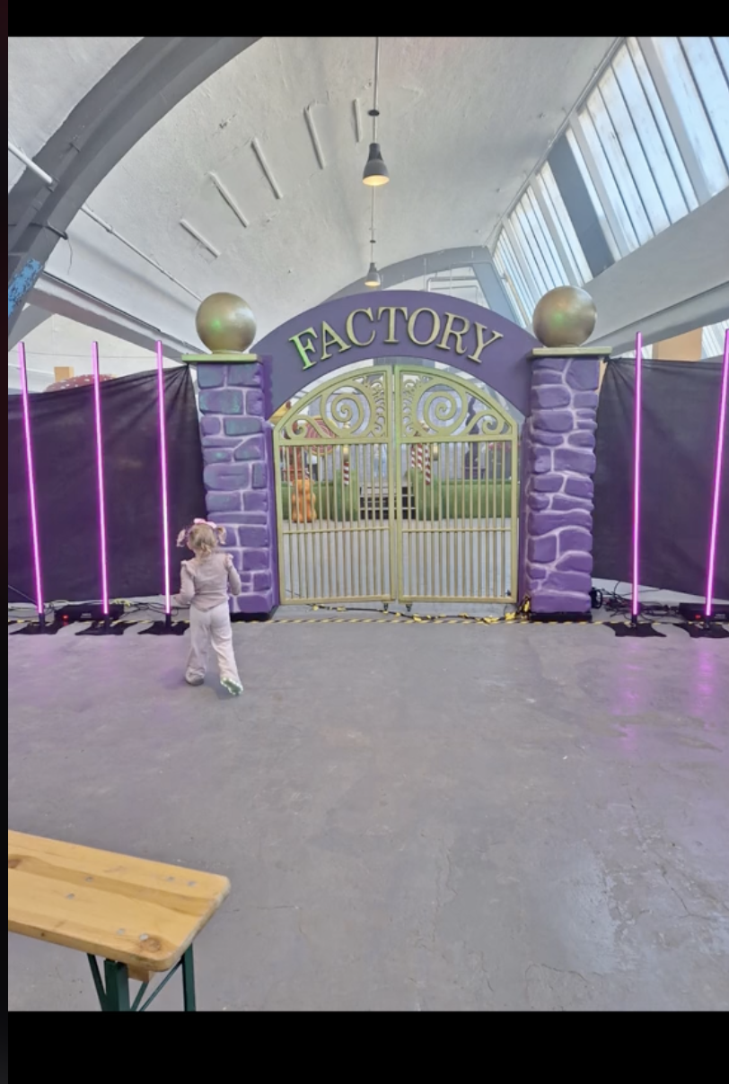 Child stands in front of gated &quot;FACTORY&quot; entrance under arched ceiling