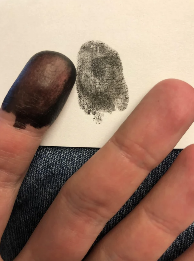 Fingerprint next to a thumbprint smudge on paper, held by a person&#x27;s hand