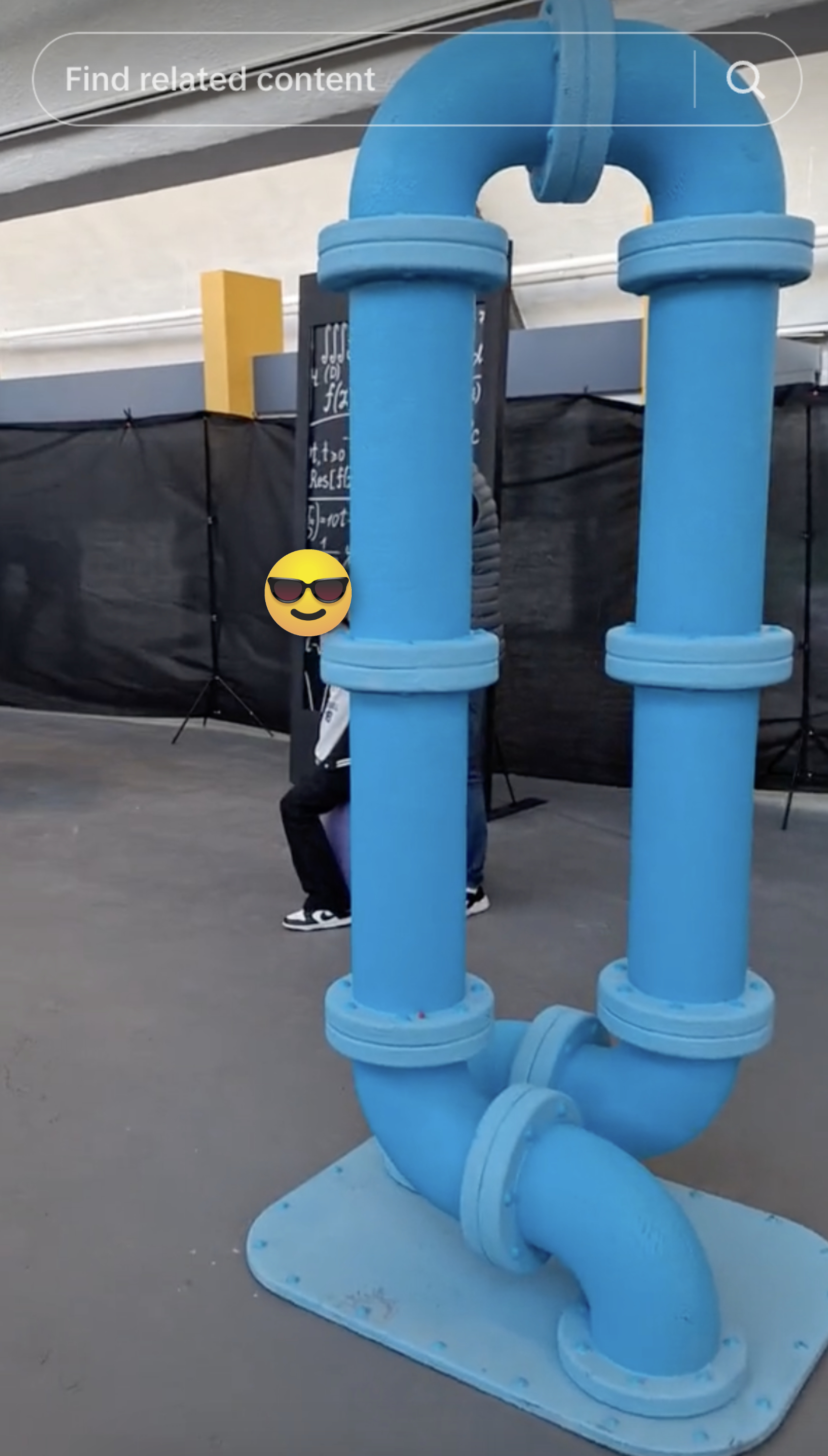 Person squats behind a large blue pipeline structure, partially concealed but visible