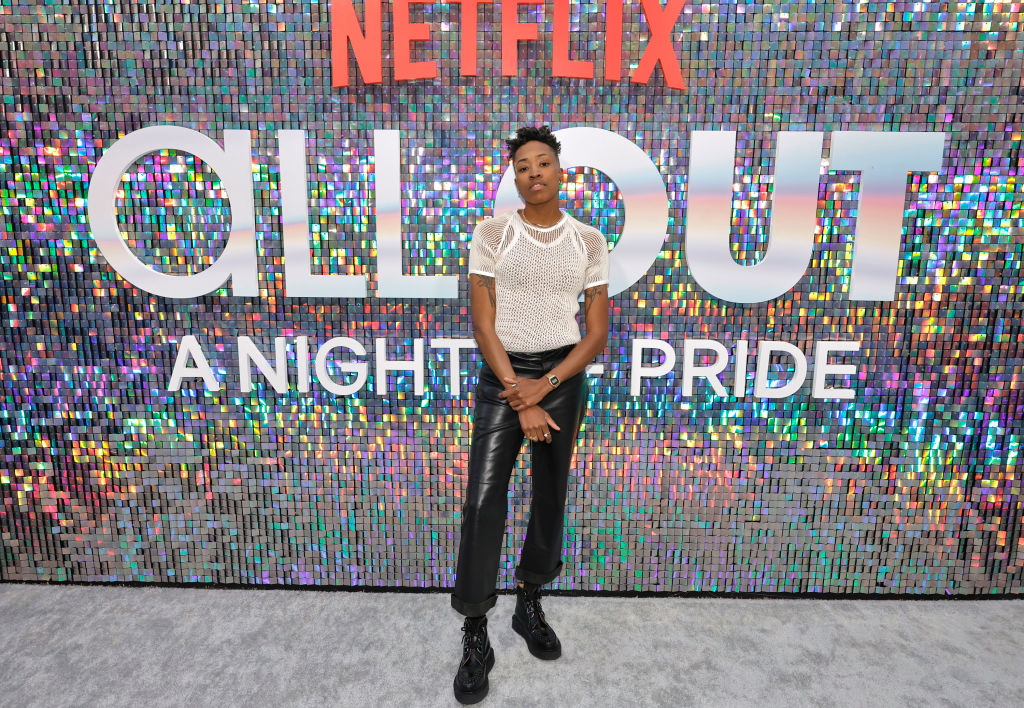 Mal Wright in a top and black pants posing at Netflix event with asequined backdrop
