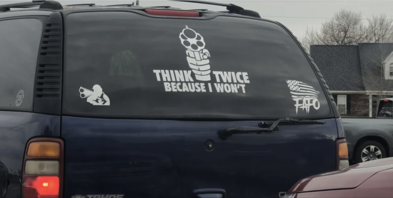 Rear window of a vehicle with decals of a gun and the text &quot;THINK TWICE BECAUSE I WON&#x27;T&quot;