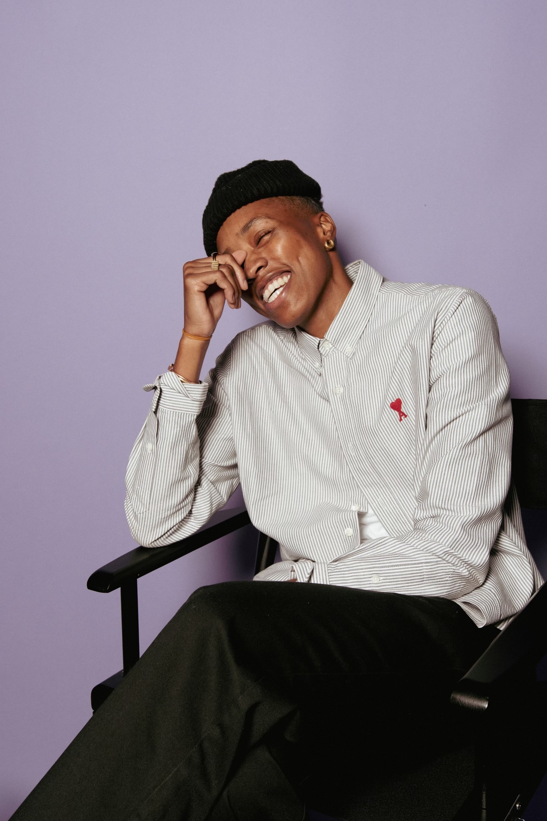 Mal Wright smiling, seated in a chair, wearing a beanie and striped shirt