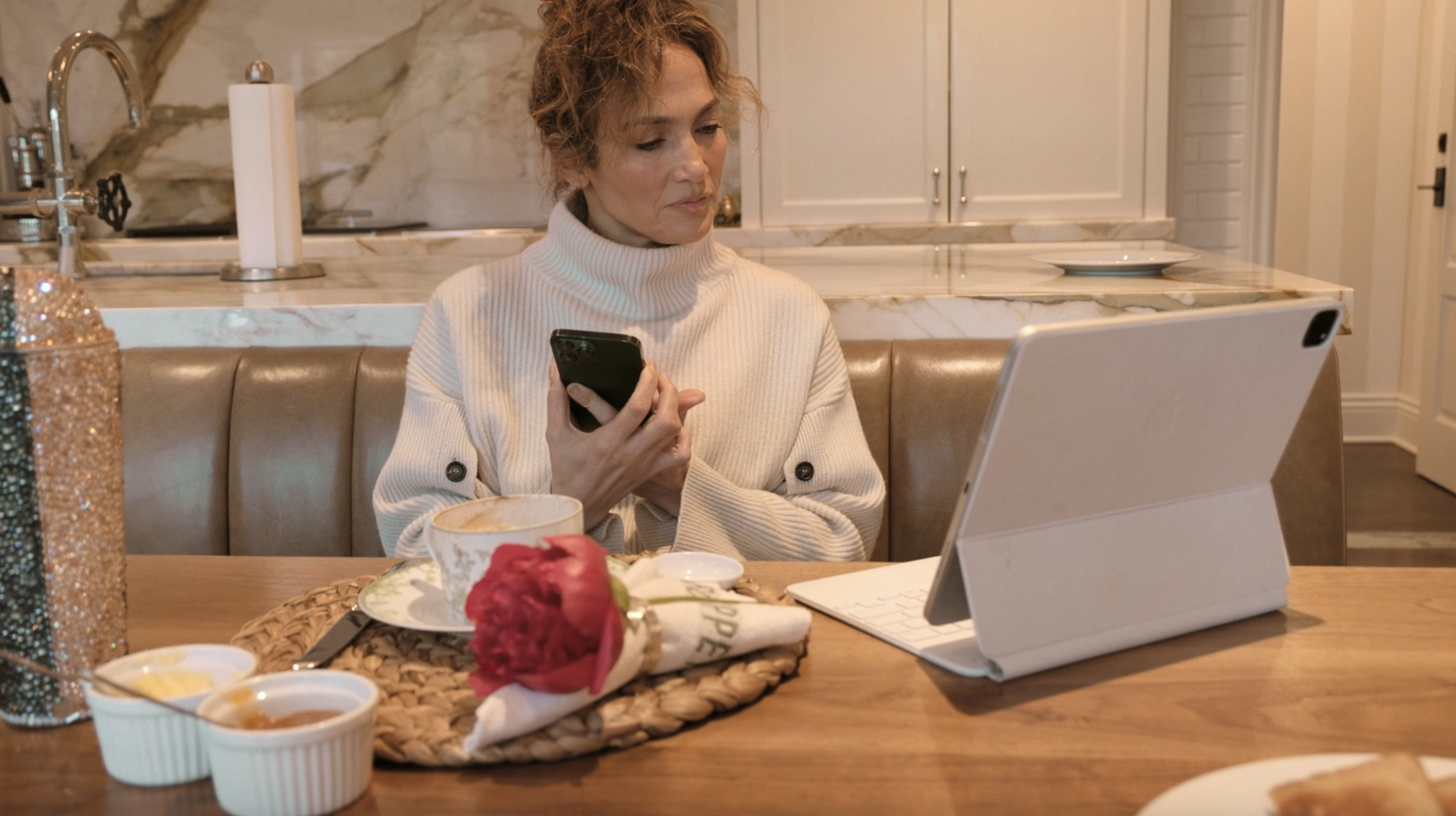 Jennifer in a turtleneck sweater speaking on the as she looks at a tablet on the table
