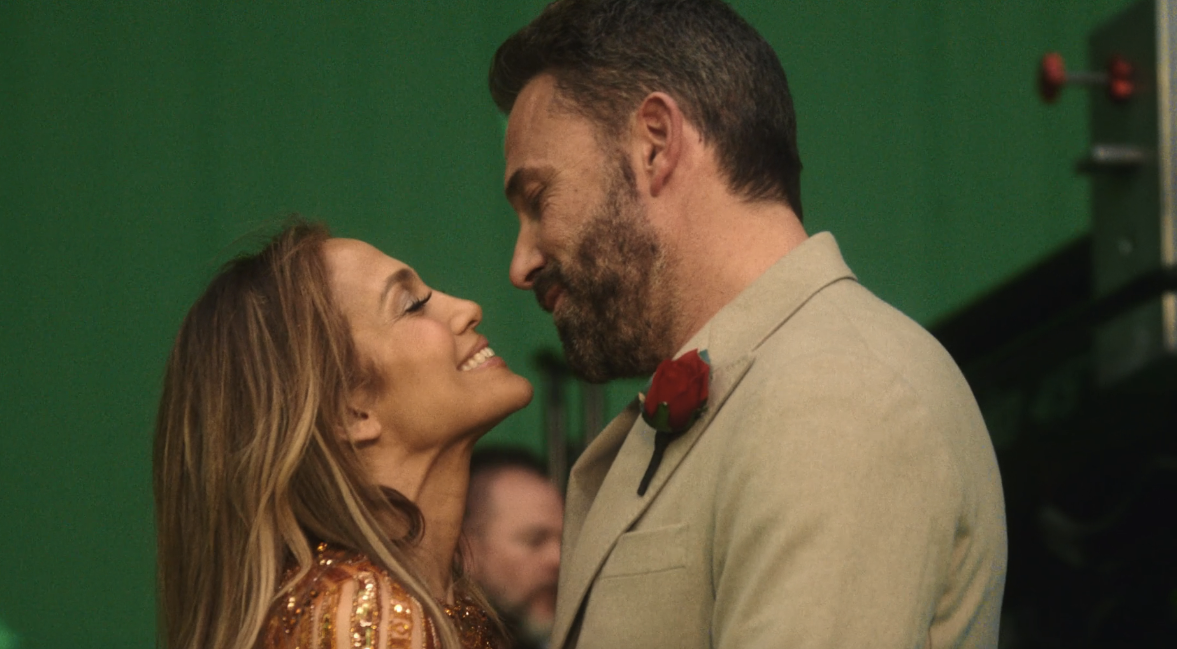 Jennifer Lopez and Ben Affleck share a smile, facing each other intimately. Lopez wears a sequined outfit, Affleck in a suit with a boutonniere