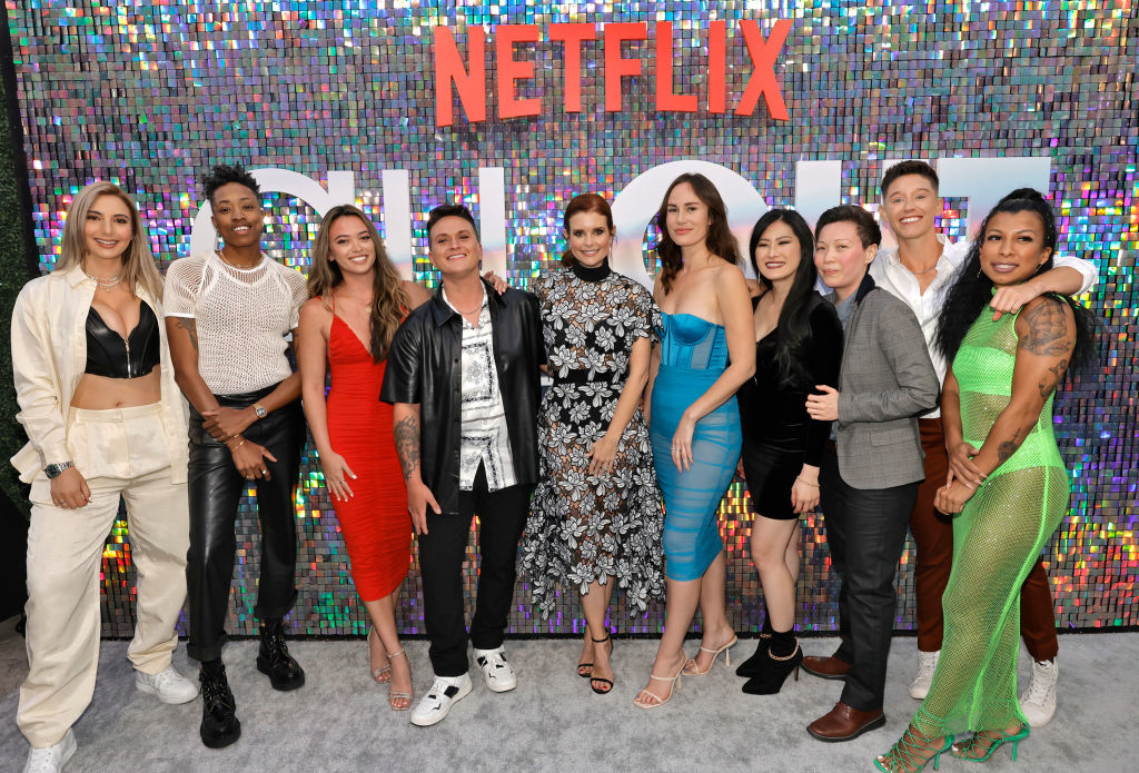 Group of nine individuals posing before a NETFLIX sign, dressed in various formal and casual attire