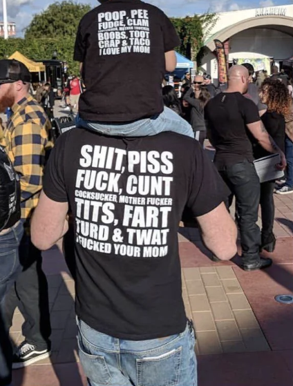 Child on parent&#x27;s shoulders; both wear profanity-laden shirts at an event. Shirt text reflects bond and humor