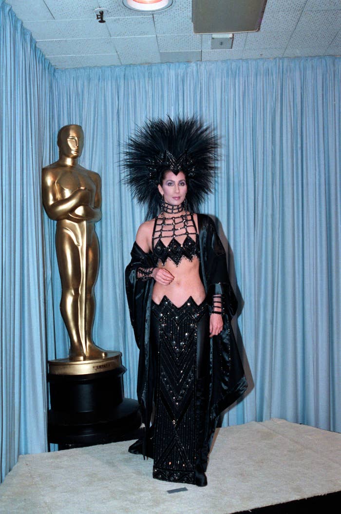 Person in extravagant black outfit with headdress next to an Oscar statue
