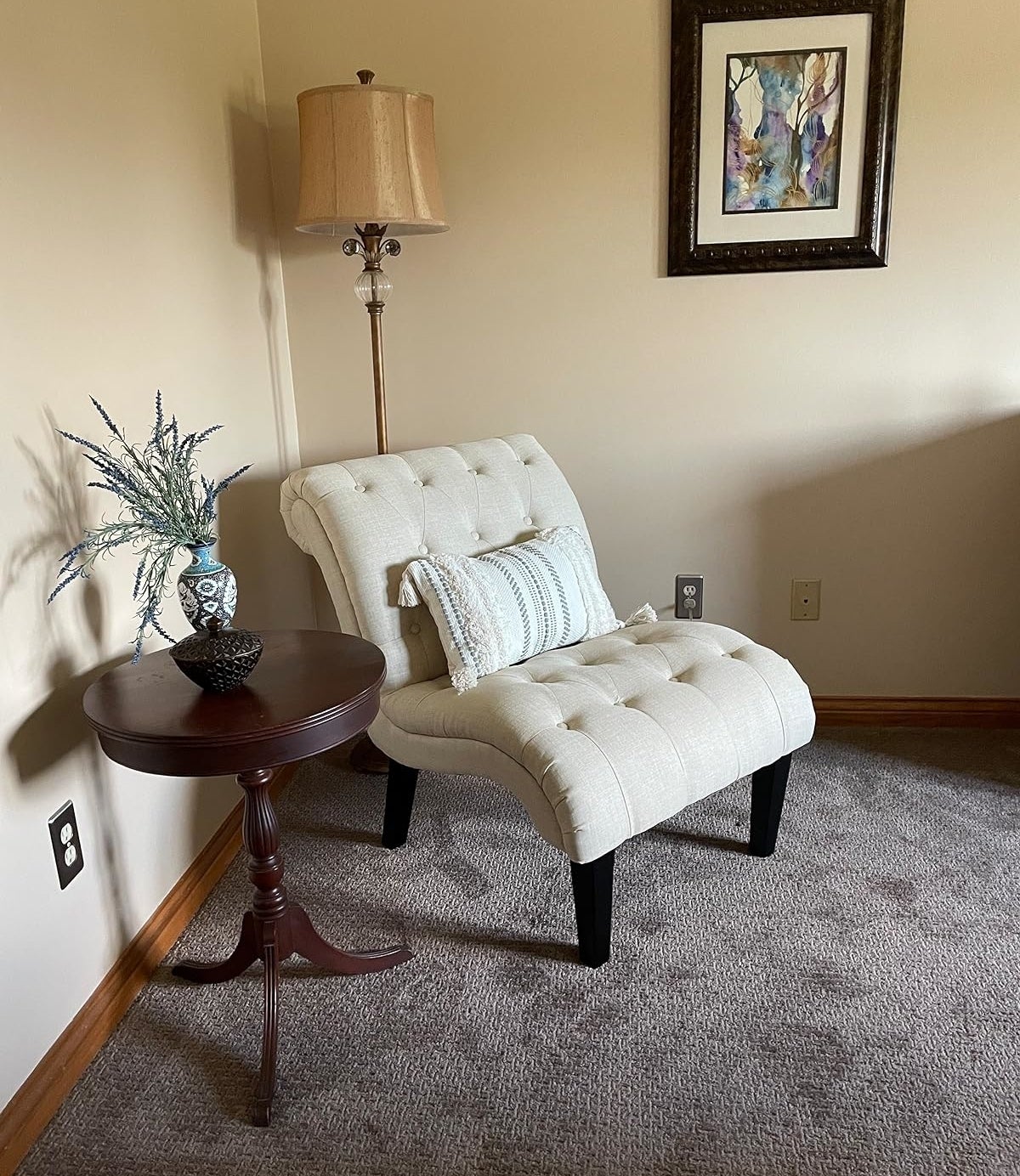 Elegant tufted armchair with beige upholstery, beside a wood side table with decorative items and a floor lamp