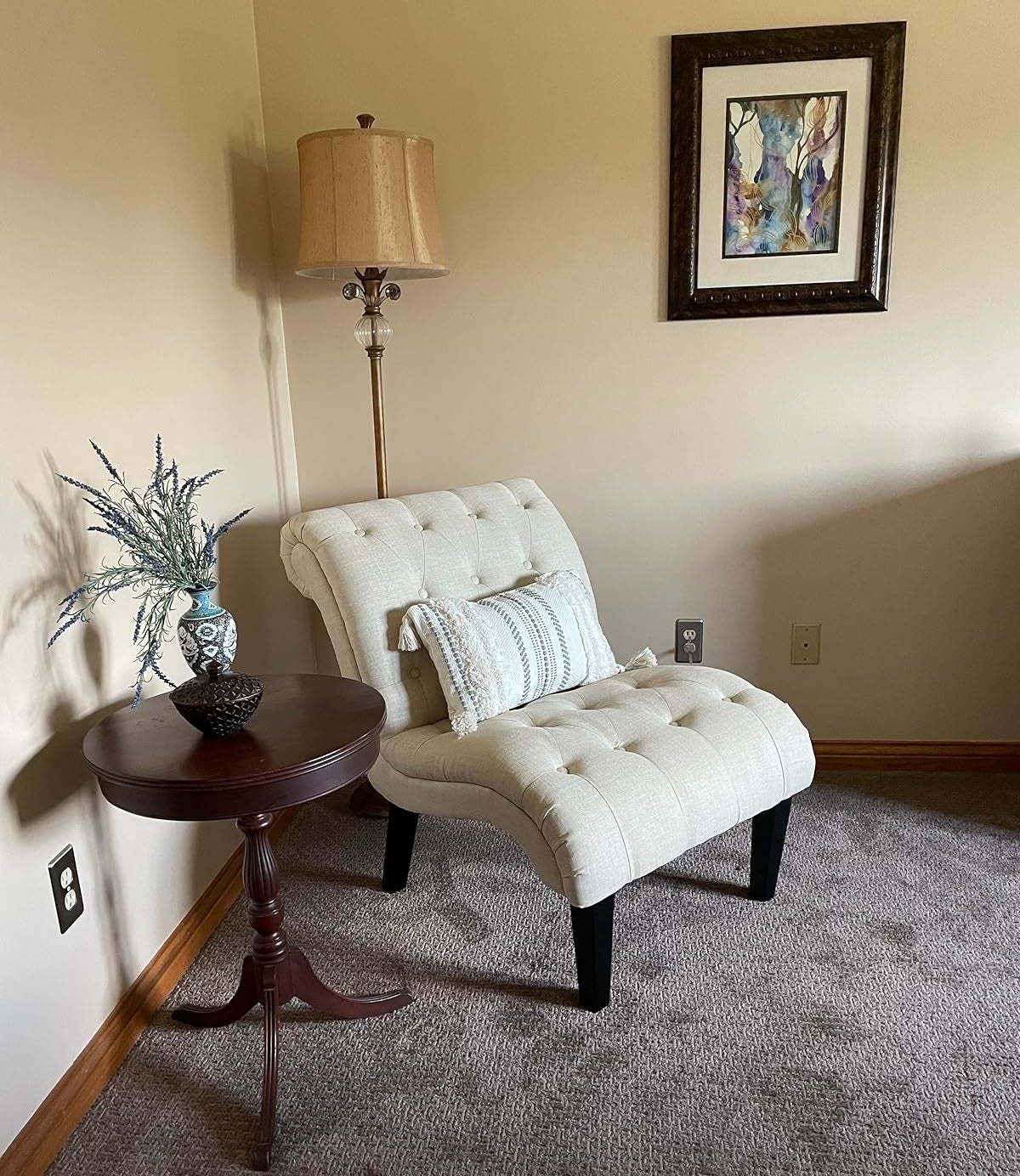 Elegant tufted armchair with beige upholstery, beside a wood side table with decorative items and a floor lamp