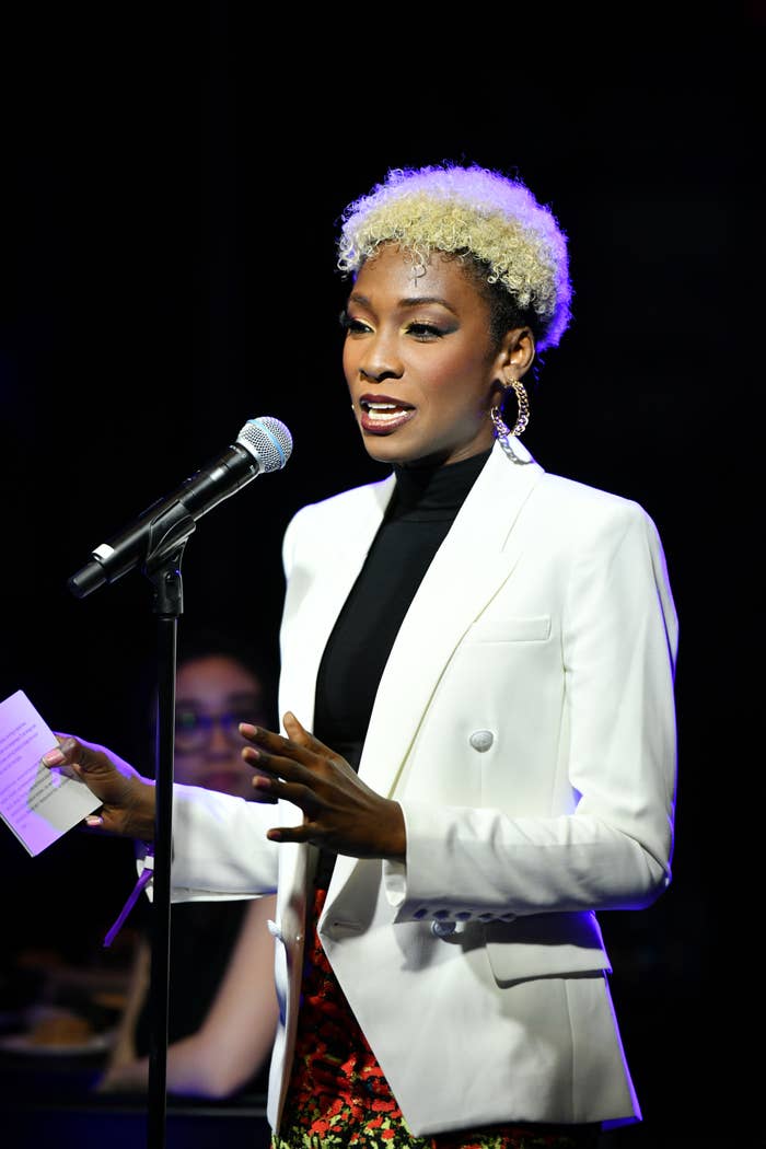 Angelica wearing a blazer and floral dress speaking into a microphone