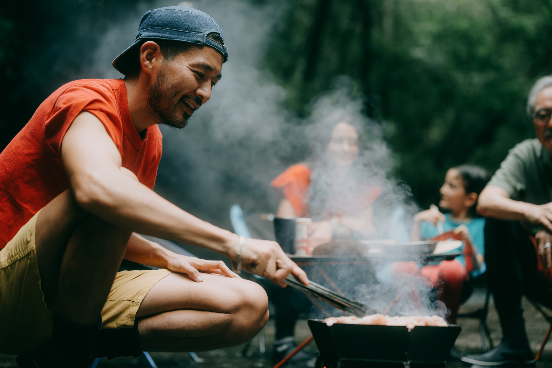 Man cooking on a grill outdoors with a group of people in a casual setting