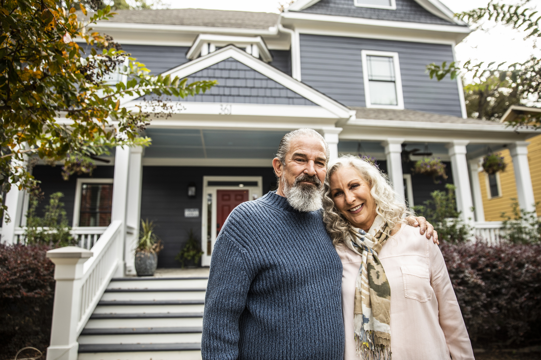 Older couple embracing and smiling in front of a house