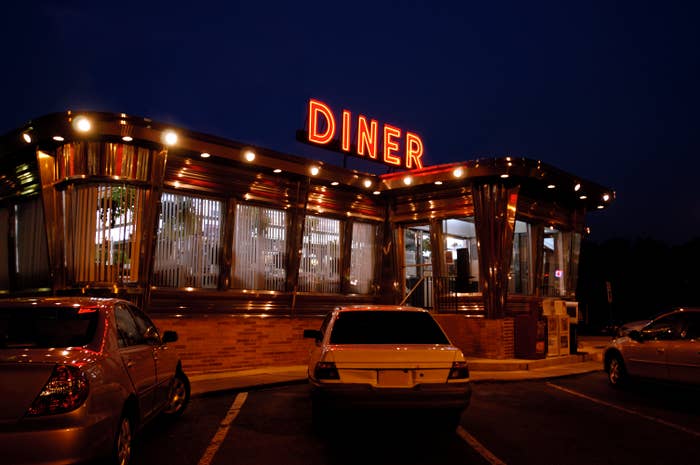 Classic diner with neon sign at dusk, parked cars in the foreground