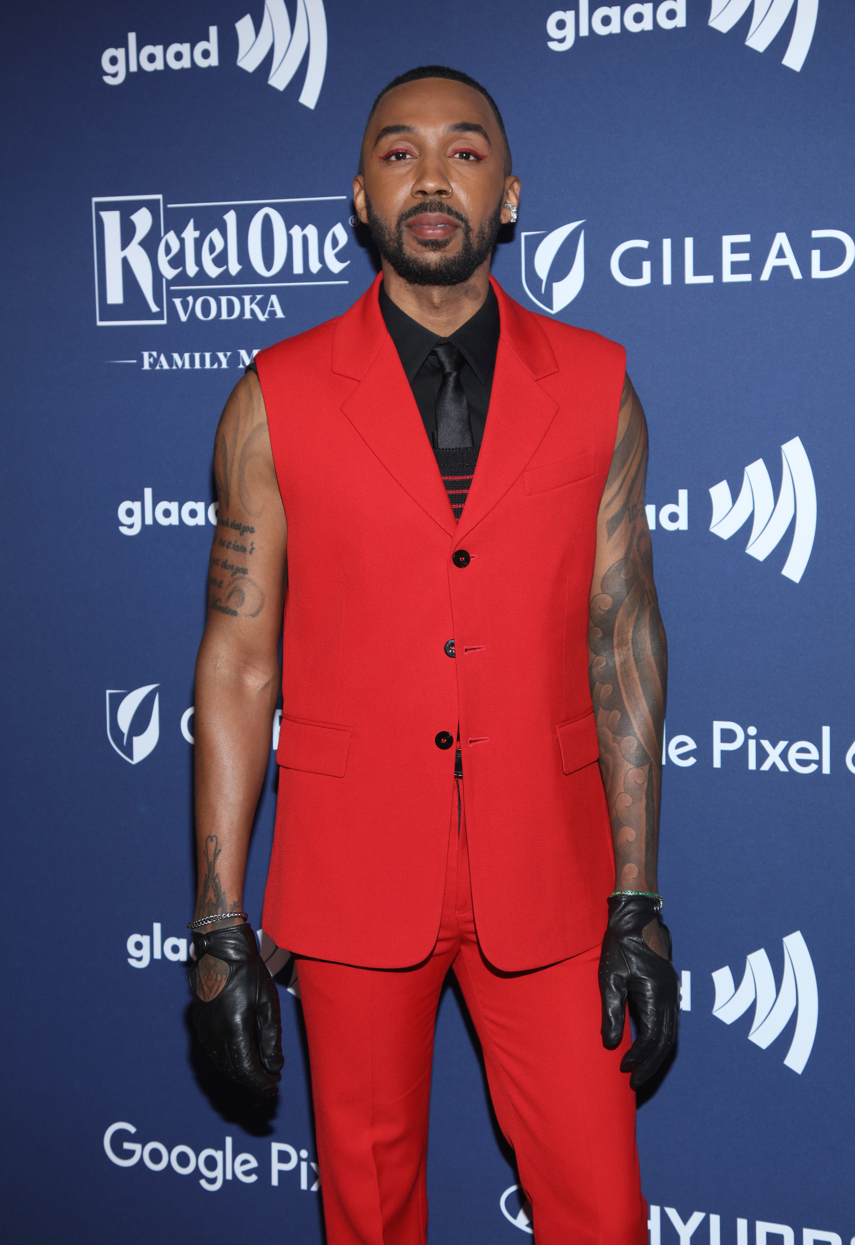 George in a sleeveless suit with shirt and gloves posing at a GLAAD event