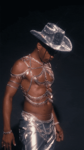 Persona con sombrero de vaquero brillante y atuendo metálico con cadenas, en pose estilizada