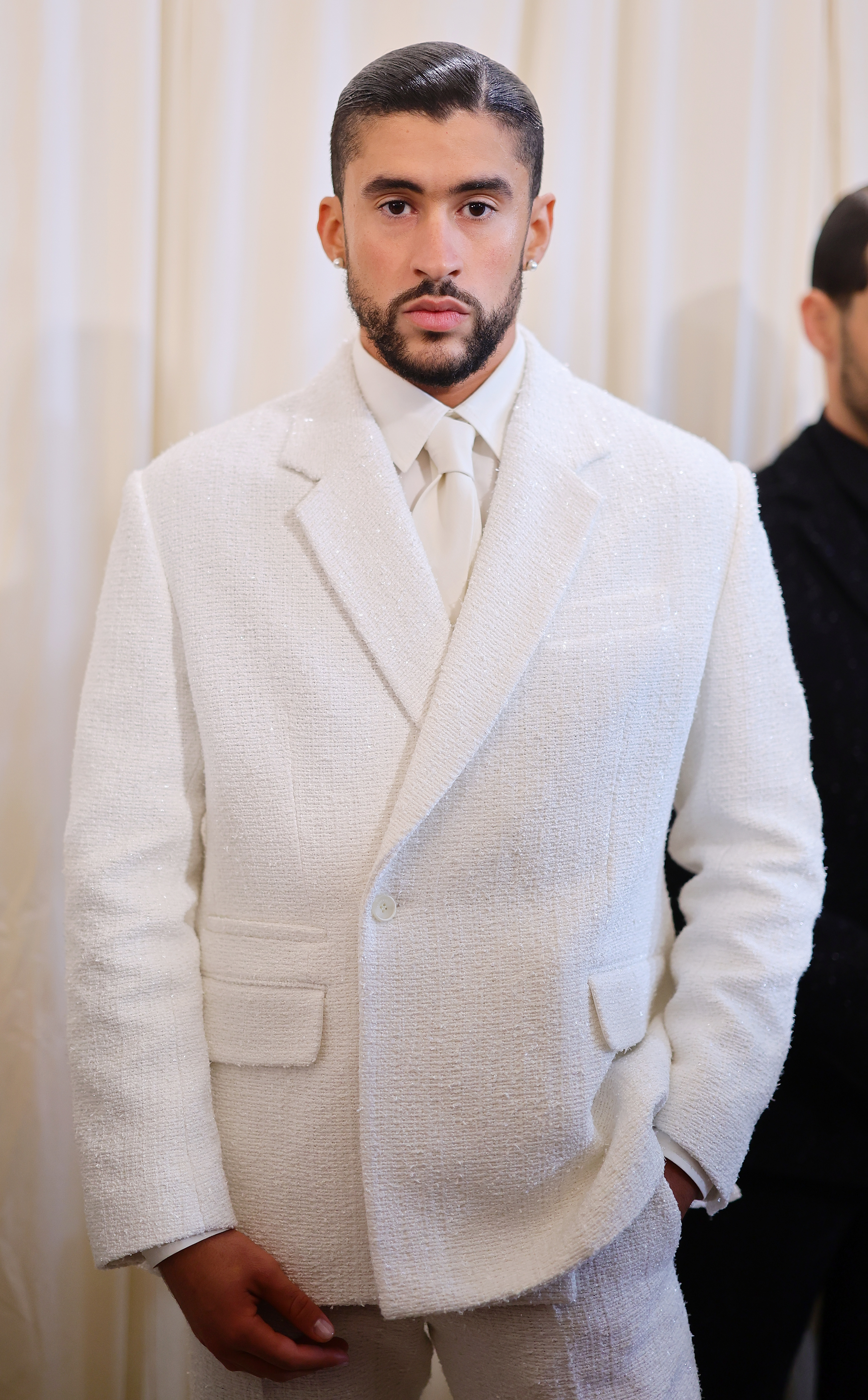 Bad Bunny in a textured suit with a matching tie, standing indoors