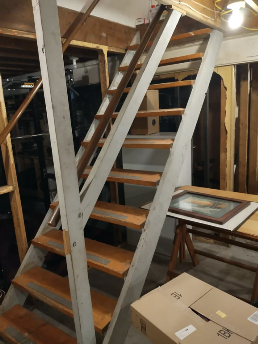 Wooden staircase with metal supports in a storage area with boxes and artwork