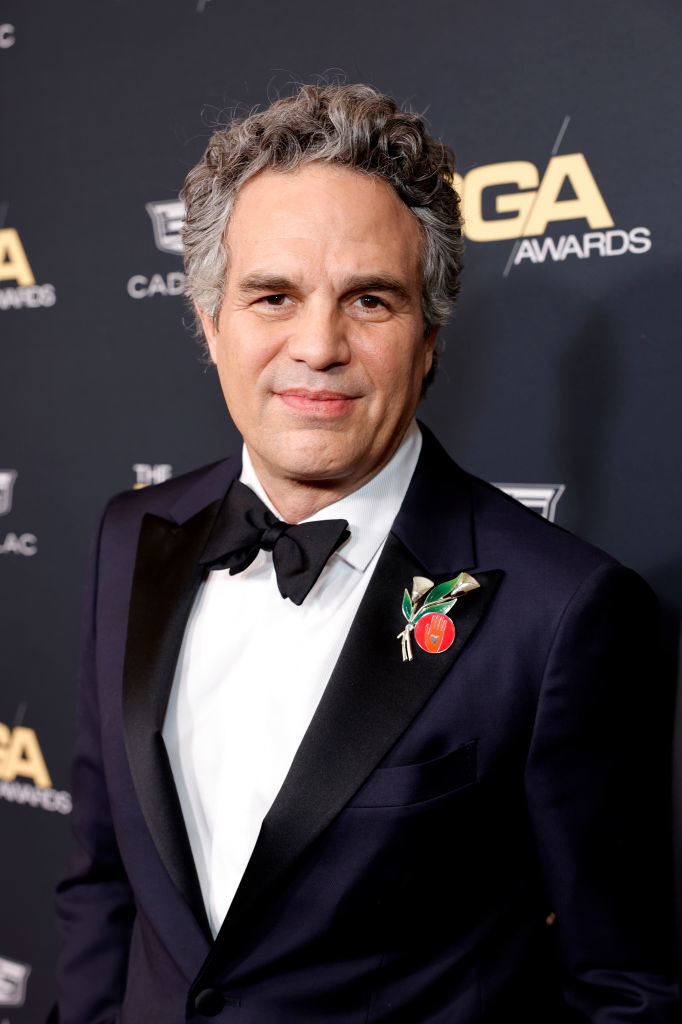 Mark in a  tuxedo with bow tie and decorative pin, smiling at event with award show backdrop