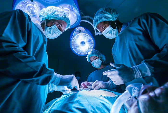 Surgeons in scrubs operate on a patient under bright surgical lights