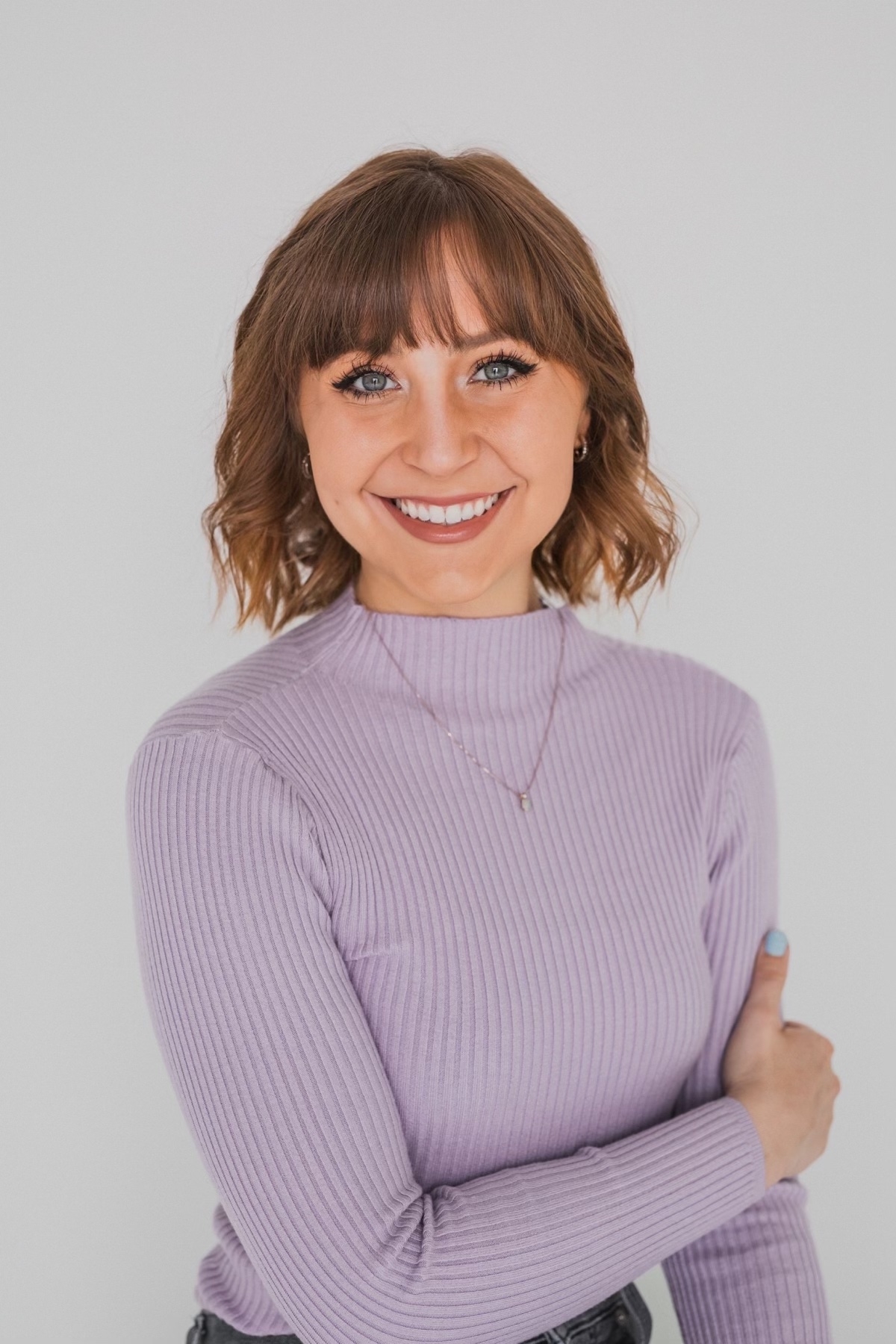 Devon, in a ribbed mock turtleneck, smiling with arms crossed