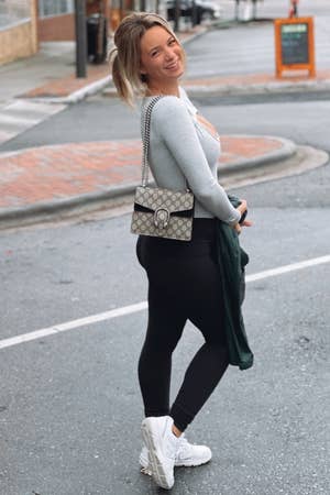 reviewer posing with a shoulder bag, wearing leggings, a cardigan, and white sneakers