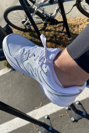 reviewer showing their white sneaker outdoors with bicycles in the background