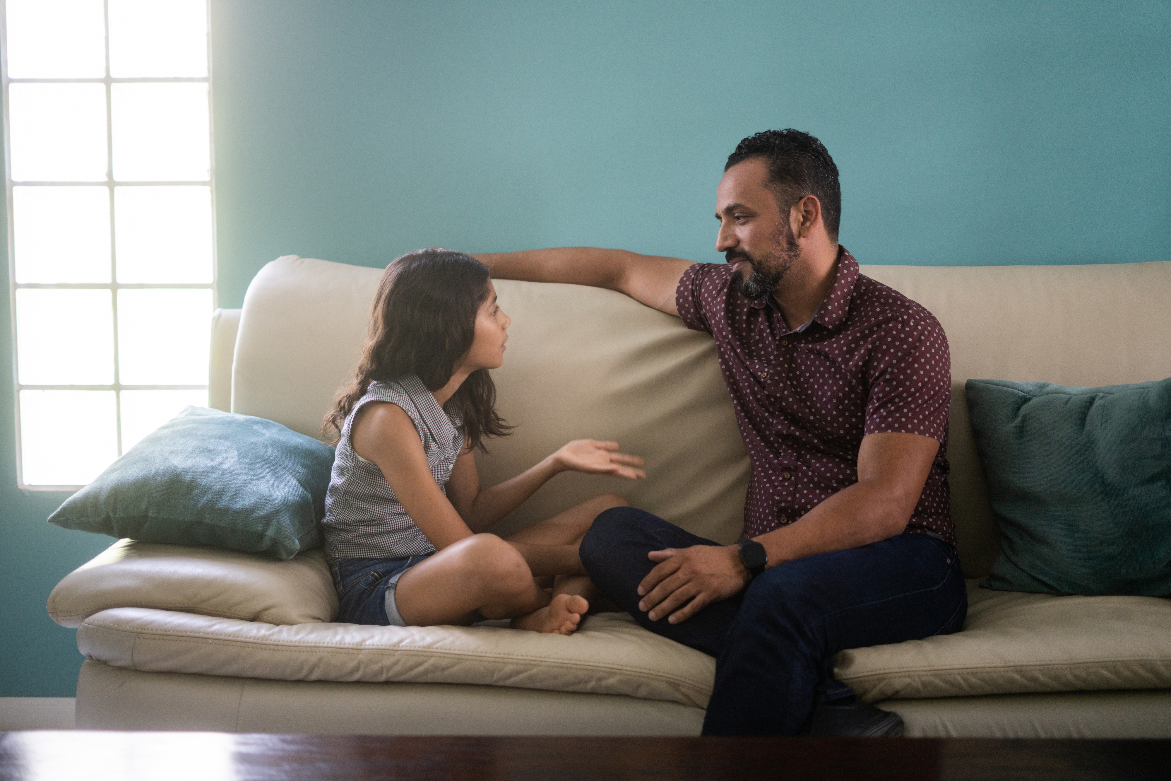 Adult and child engage in conversation on a couch, expressing gestures of communication