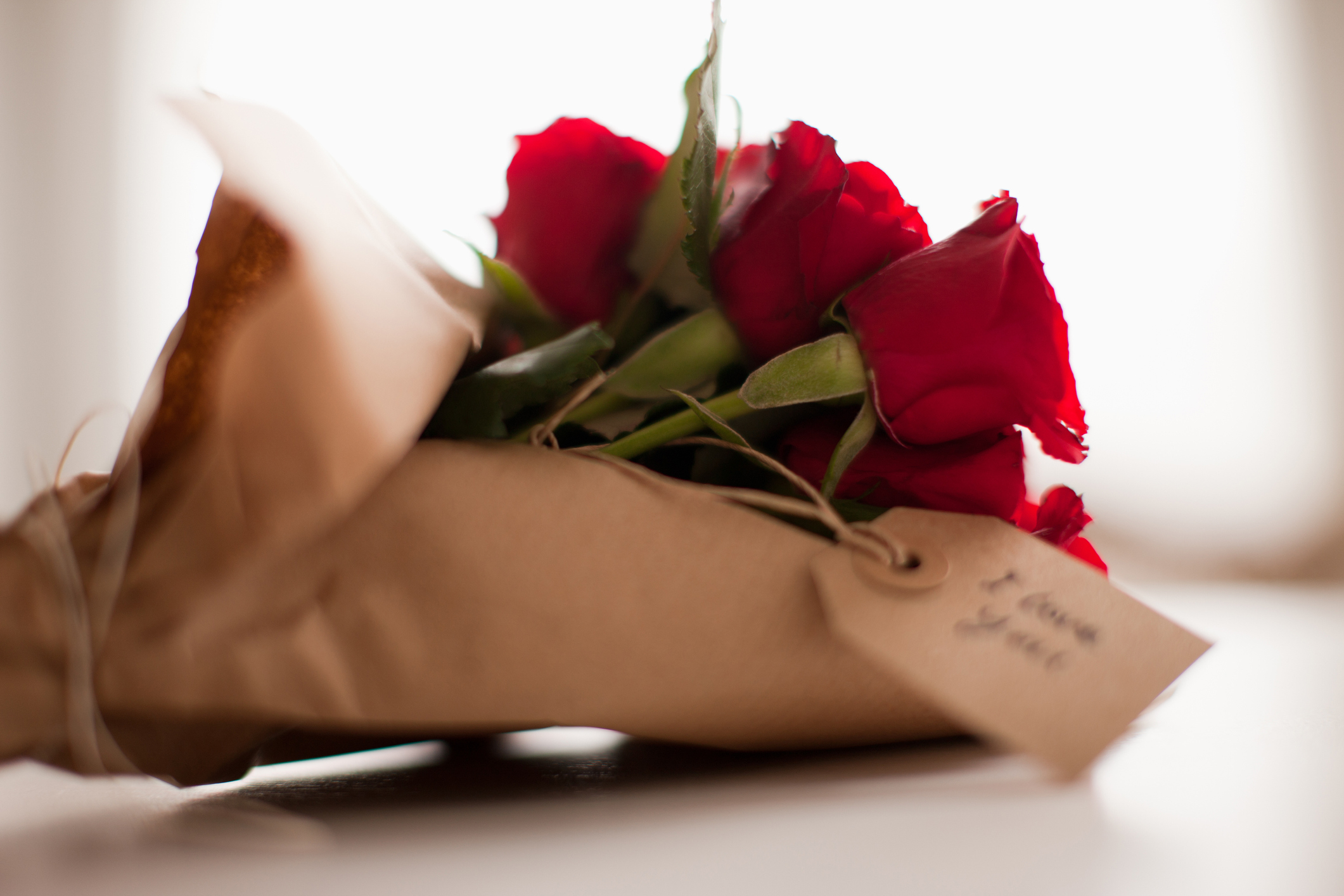 Bouquet of red roses wrapped in paper with a tag, possibly a romantic gift